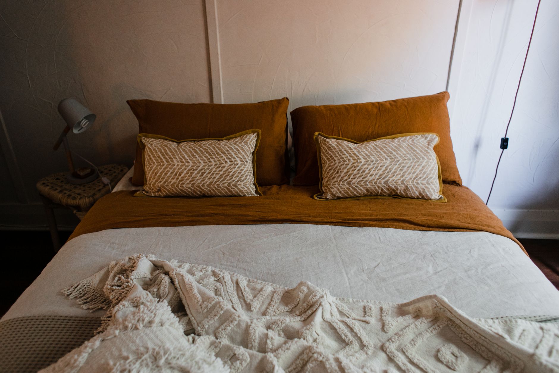 A bed dressed in warm rust linen with a textured cream throw
